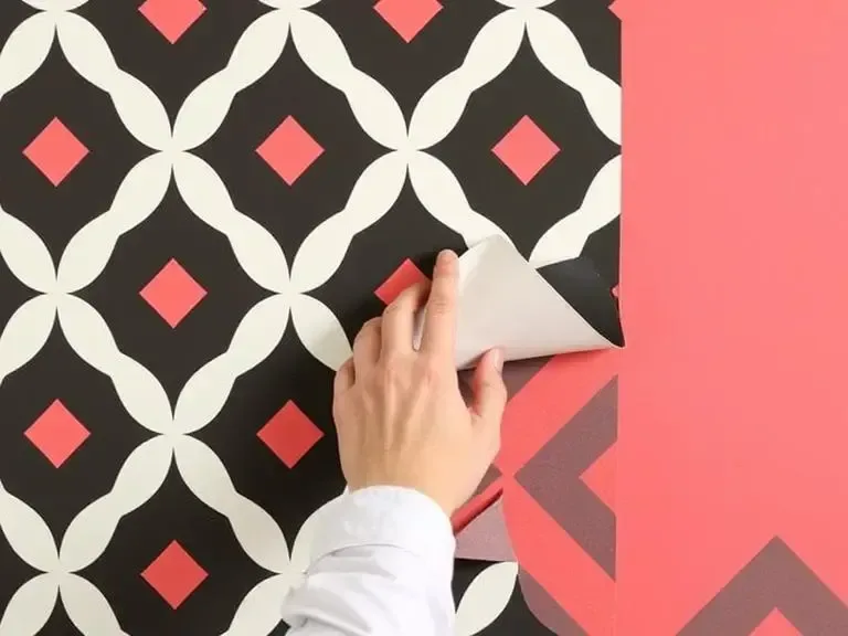 A hand applying peel-and-stick wallpaper to a wall with a bold geometric pattern.